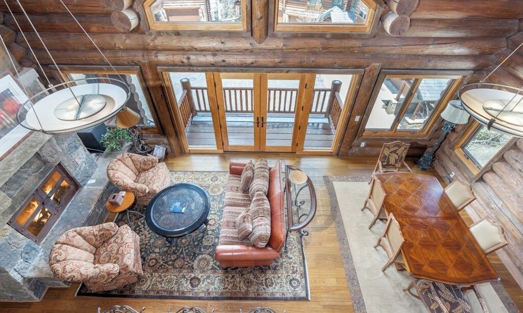 A log cabin interior with a fireplace, seating area, dining table, and large windows.