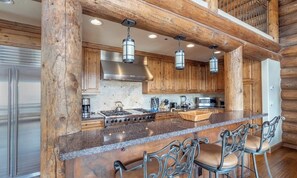 A kitchen with wooden cabinets, a granite countertop, and a bar area with metal chairs. - Gorgeous mountain home with balcony, fireplace & views (Mountain Village)