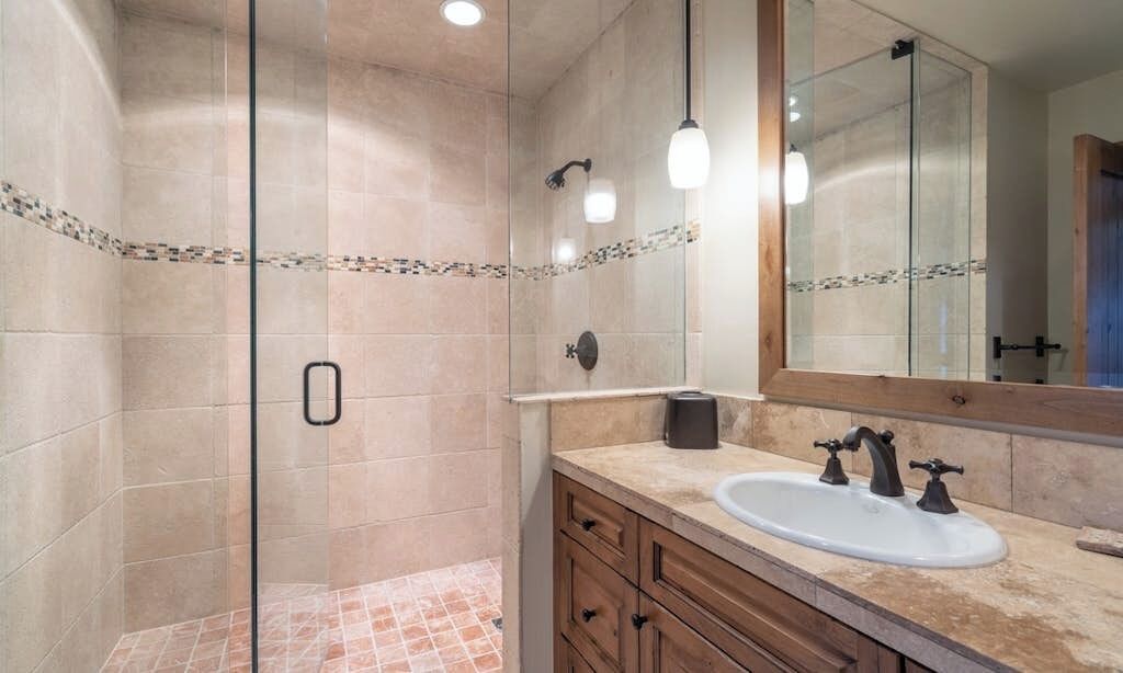 A bathroom with a glass shower enclosure, a sink with a mirror, and a tiled floor.