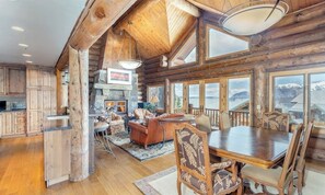 A log cabin interior with a dining area, kitchen, and living room with large windows. - Gorgeous mountain home with balcony, fireplace & views (Mountain Village)