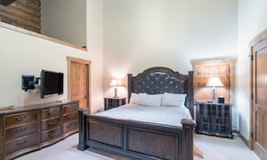 A bedroom with a large bed, wooden dresser, bedside tables, a television, and a wooden door. - Gorgeous mountain home with balcony, fireplace & views (Mountain Village)