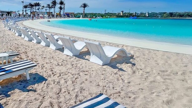 Uma praia com cadeiras de banho brancas, mar azul cristalino e palmeiras.
