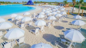 Uma praia com guarda-sóis brancos e espreguiçadeiras, uma piscina e um tobogã aquático.