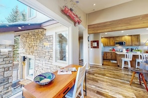 A modern kitchen with wooden cabinets, a stone wall, and a dining area with a wooden table and chairs. - Four-story home with amazing mountain/golf view, fireplace & Ping-Pong (Avon)