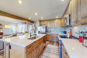 A modern kitchen with wooden cabinets, a large island, stainless steel appliances, and a tiled backsplash. - Four-story home with amazing mountain/golf view, fireplace & Ping-Pong (Avon)