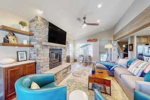 A living room with a stone fireplace, blue armchairs, a sofa, a wooden coffee table, and a television mounted on the wall. - Four-story home with amazing mountain/golf view, fireplace & Ping-Pong (Avon)