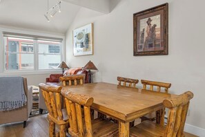 Ein Essbereich mit einem Holztisch und Stühlen, einem gerahmten Bild an der Wand und einem Fenster mit Jalousien.
