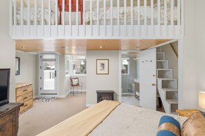 Ein Schlafzimmer mit Schlafgalerie, einem Fernseher, einem Kamin und einer Treppe.