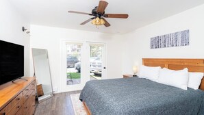 Une chambre à coucher comprenant un lit, un ventilateur de plafond, une télévision, une commode et une porte donnant sur l’extérieur.