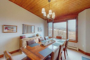 Ein Essbereich mit Holztisch, Stühlen, einer Kandelaber und großen Fenstern mit Blick.