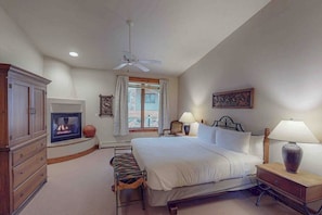 Ein Schlafzimmer mit Bett, Nachttischlampen, Kamin, Bank und Deckenventilator.