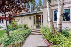 Ein Haus mit einer Haustür, Stufen, die davor liegen, und einem Garten mit verschiedenen Pflanzen und Bäumen.