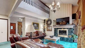 Un salón amplio con sofás de cuero, chimenea, televisor y escalera.