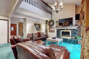 Ein geräumiges Wohnzimmer mit Ledersofas, einem Kamin, einem Fernseher und einer Treppe.