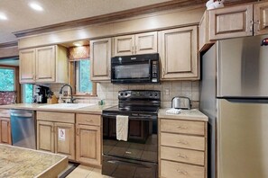 Eine Küche mit Holzausstattung, einem Edelstahlkühlschrank, einer Mikrowelle, einem Backofen und einem Geschirrspüler.