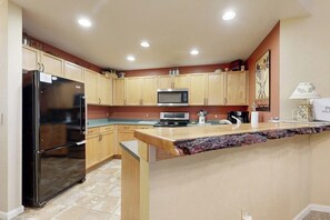 A kitchen with wooden cabinets, a black refrigerator, a microwave, and a granite countertop. - Riverfront gem with loft & stunning water views, near skiing (Edwards)
