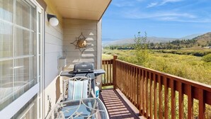 Ein Balkon mit Grill, einem Glastisch und Blick auf eine grüne Landschaft.