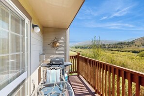 A balcony with a grill, a glass table, and a view of a green landscape. - Riverfront gem with loft & stunning water views, near skiing (Edwards)