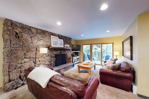A living room with a stone wall, leather sofas, a fireplace, and a television. - Beaver Creek West Condo with Heated Pool, 3 Hot Tubs & Shuttle to the Slopes (Avon)