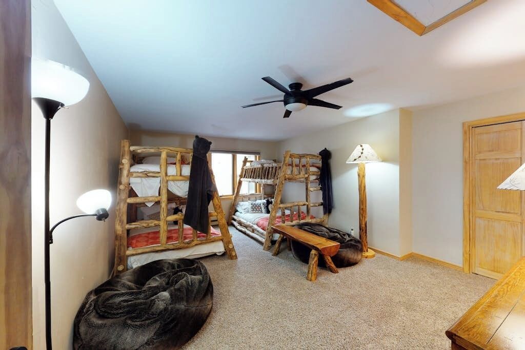 A room with bunk beds, a ceiling fan, a lamp, and a wooden door.