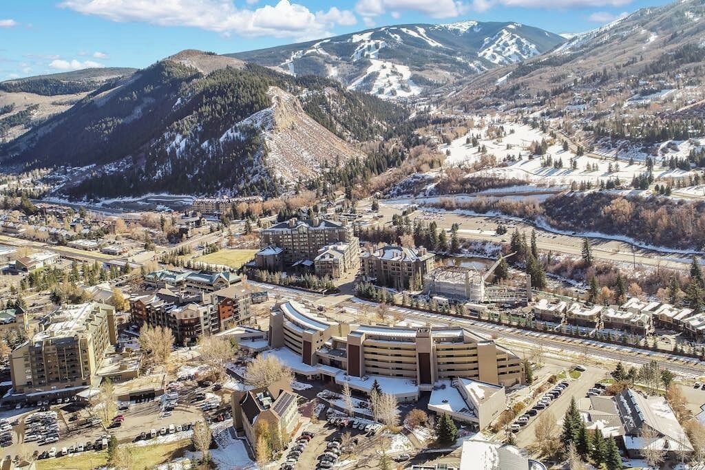 A hotel with a central parking area, surrounded by buildings and a mountainous backdrop.