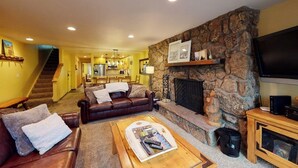 A living room with a stone fireplace, a television, and a sofa. - Beaver Creek West Condo with Heated Pool, 3 Hot Tubs & Shuttle to the Slopes (Avon)