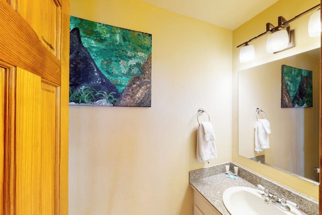 Een badkamer met een granieten aanrechtblad, een witte wasbak, een spiegel en twee handdoeken die aan haken hangen.