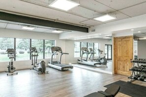Ein Fitnessraum mit Laufbändern, Crosstrainern und einem Gewichtsständer.