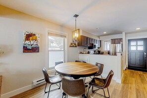A modern kitchen with a dining area, wooden flooring, and a painting on the wall. - Golf Course Condo with Gas Fireplace, WiFi & Deck with Mountain Views (Avon)