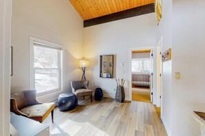 A room with a wooden floor, a sofa, a chair, a lamp, and a mirror on the wall. - Golf Course Condo with Gas Fireplace, WiFi & Deck with Mountain Views (Avon)