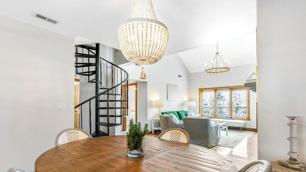 Een eethoek met een ronde houten tafel, een kroonluchter en een spiltrap op de achtergrond.