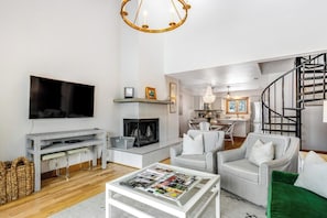 Ein modernes Wohnzimmer mit Flachbildfernseher, Kamin, Essbereich und einer Treppe.