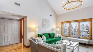 Een woonkamer met een groene bank, grijze fauteuils, een salontafel en een groot raam met uitzicht op met sneeuw bedekte bomen.