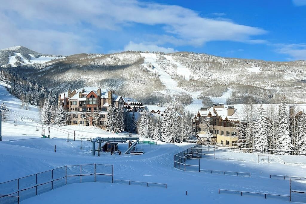 Een met sneeuw bedekte wintersportplaats met een chalet, skipistes en een berg op de achtergrond.