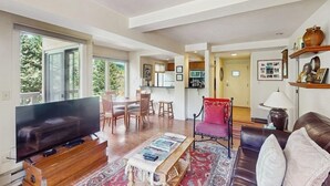 Ein Wohnzimmer mit Fernseher, Couchtisch aus Holz, einem roten Sessel und einer Couch.