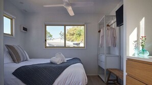 Ein Schlafzimmer mit Bett, Fenster, Deckenventilator, Kleiderschrank und einer Sitzbank.
