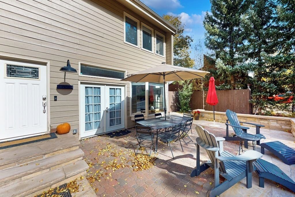 A patio with a table and chairs, a red umbrella, and a wooden fence.