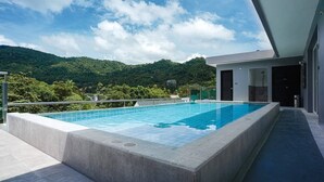 Une piscine moderne offrant une vue sur des collines verdoyantes, un espace abrité avec une porte et un ciel dégagé.