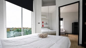 Une chambre d’hôtel moderne avec un grand lit, une vue par la fenêtre et un coin salon séparé.