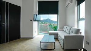 Un salon moderne avec un canapé, une table basse, un téléviseur et une grande fenêtre donnant sur une montagne.