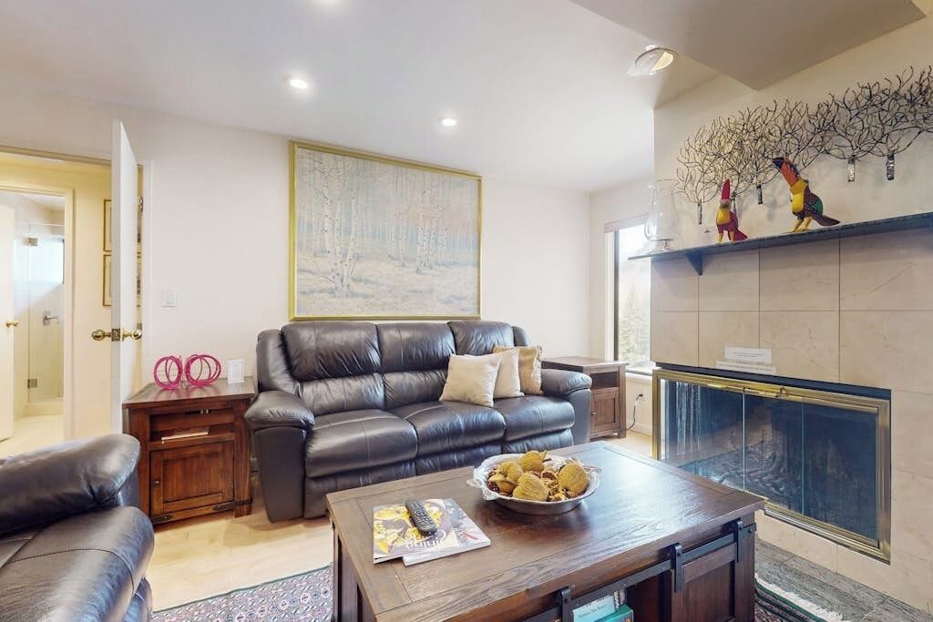 Una sala de estar con un sofá de cuero, una mesa de centro con revistas, una chimenea con adornos y un cuadro en la pared.