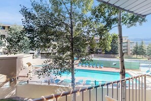 Ein Poolbereich mit Liegestühlen, einem Tennisplatz und einem Gebäude mit Balkonen.