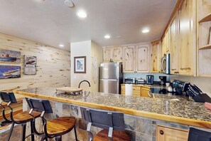 Eine Küche mit Holzschränken, Granit-Arbeitsplatten, einem Edelstahlkühlschrank und einer Bar mit Barhocker.