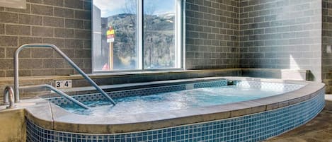 A hot tub with a tiled edge, a metal ladder, and a window with a view of a building and trees.