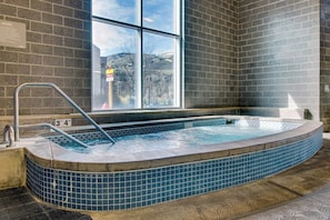 Ein Whirlpool mit gefliestem Rand, einer Metallleiter und einem Fenster mit Blick auf ein Gebäude und Bäume.