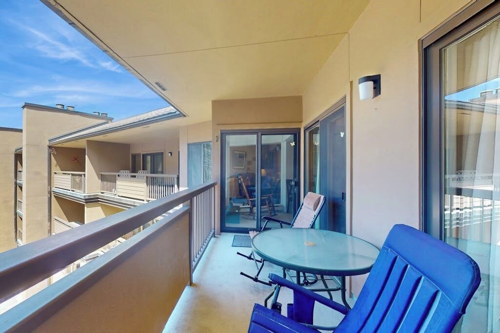 Ein Balkon mit Glastisch und Stühlen, einer Schiebetür und Blick auf andere Gebäude.