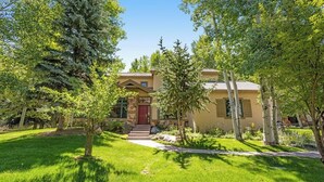 Une maison à deux étages avec une porte rouge, entourée d’une pelouse bien entretenue et d’arbres.