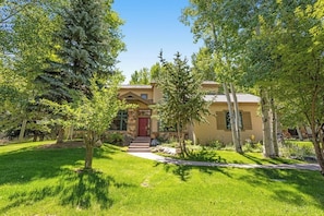 A two-story house with a red door, surrounded by a well-maintained lawn and trees. - Spacious Home w/Mountain Views, Game Room, Shared Hot Tub, Grill, & Pool Table (Edwards)