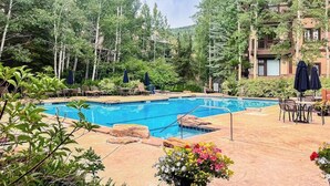 Une piscine entourée d’arbres, avec des chaises longues et des parasols.