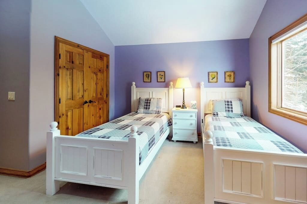 Een slaapkamer met twee bedden, een houten deur, een raam en een nachtkastje met een lamp.